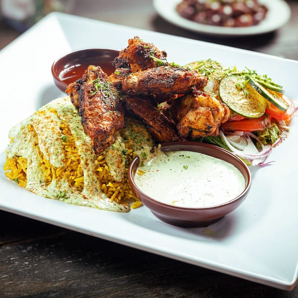 Mediterranean chicken wings with yellow rice, salad, and two dipping sauces on a white plate.