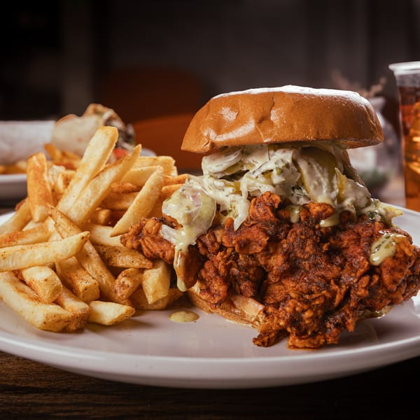 Crispy fried chicken sandwich with sauce, pickles, and coleslaw, served with seasoned fries.