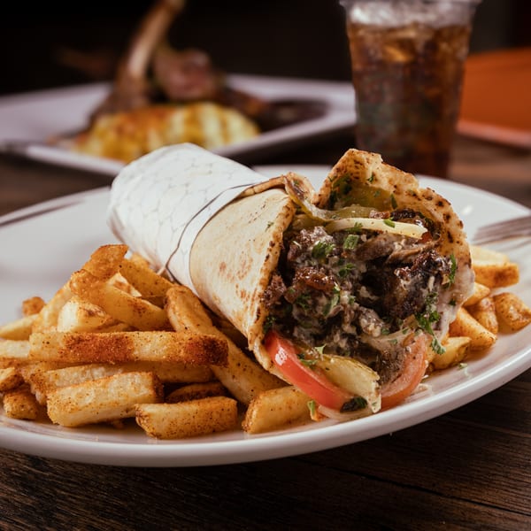 EZ Eatz by Yaya's Mediterranean shawarma wrap with fries and a drink on a wooden table.