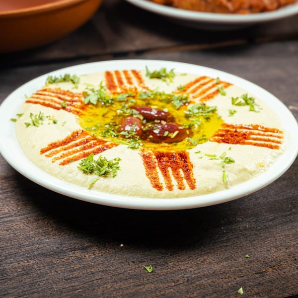 Creamy hummus topped with olive oil, parsley, paprika, and whole olives on a white plate.