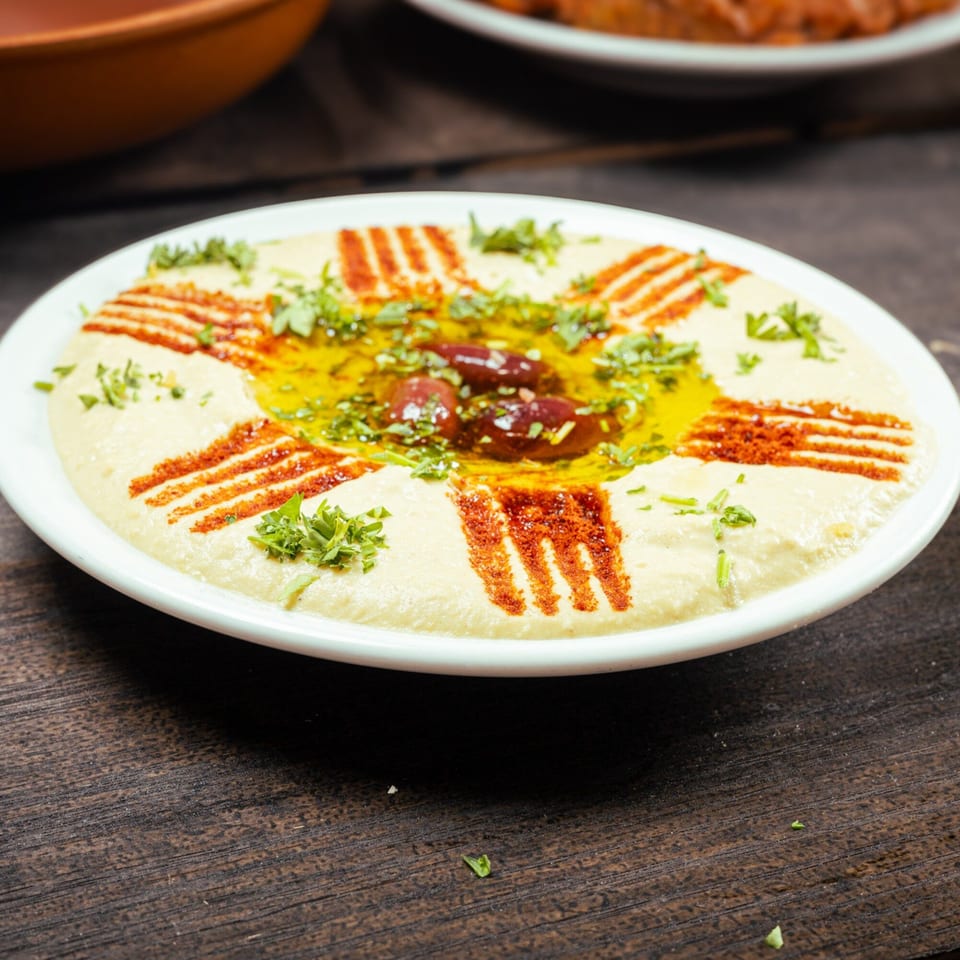 Creamy hummus topped with olive oil, parsley, paprika, and whole olives on a white plate.