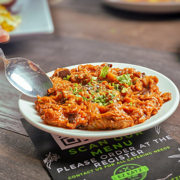 A spoon scoops a vibrant orange Mediterranean dish, garnished with fresh herbs, from a white plate.